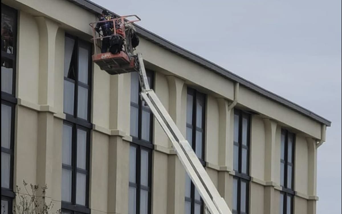 Boom lift raised to a commercial building roofline for exterior caulking repair