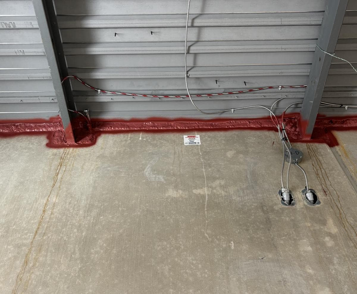 Red firestop sealant applied at wall-floor junction with electrical conduit penetrations